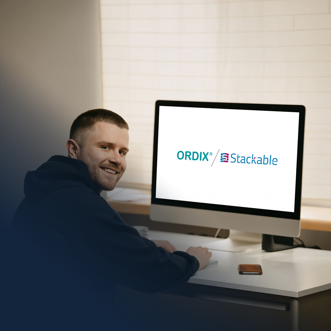 Junger IT-Mitarbeiter sitzt an Laptop mit ORDIX und Stackable Logo darauf