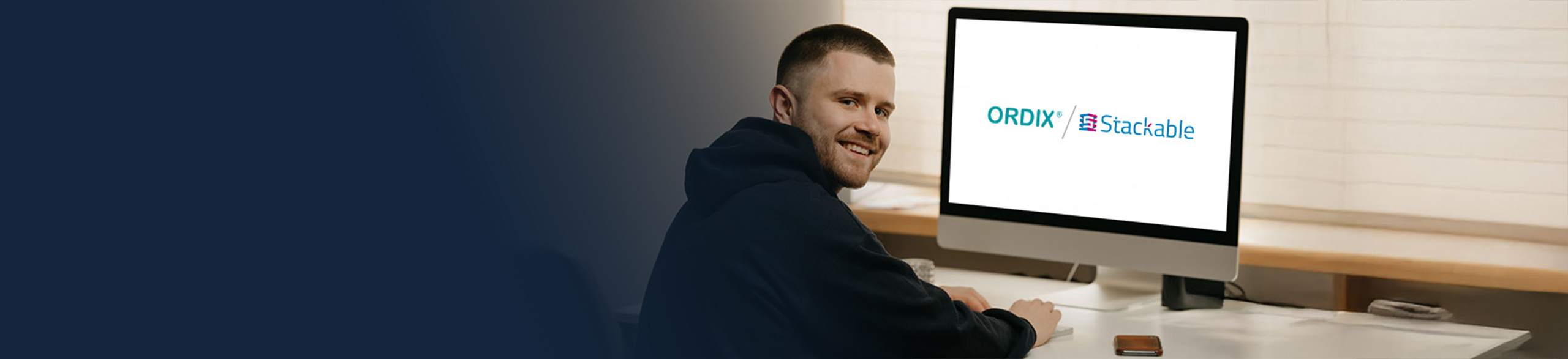 Junger IT-Mitarbeiter sitzt an Laptop mit ORDIX und Stackable Logo darauf